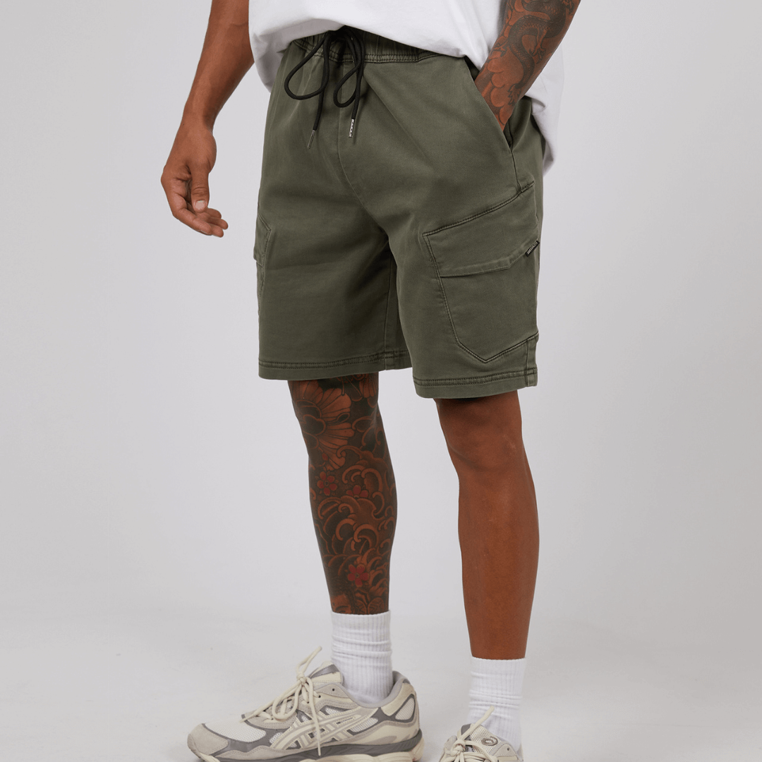 Stewarts Menswear St Goliath Gully Cargo shorts. The inset cargo pockets, waist band, and side pockets make these hybrid denim shorts a must-have for any adventure. Photo shows front view of model wearing St Goliath Gully Cargo Short. Colour is Khaki