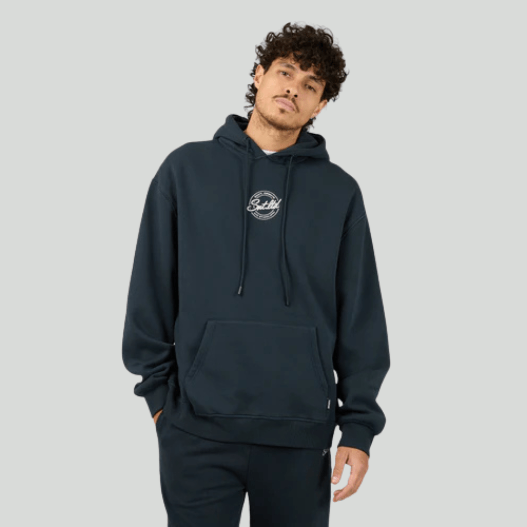Man wearing a navy hoodie with a St. Goliath logo on a gray background. St Goliath Radio Hoodie available from Stewarts Menswear, Mullumbimby