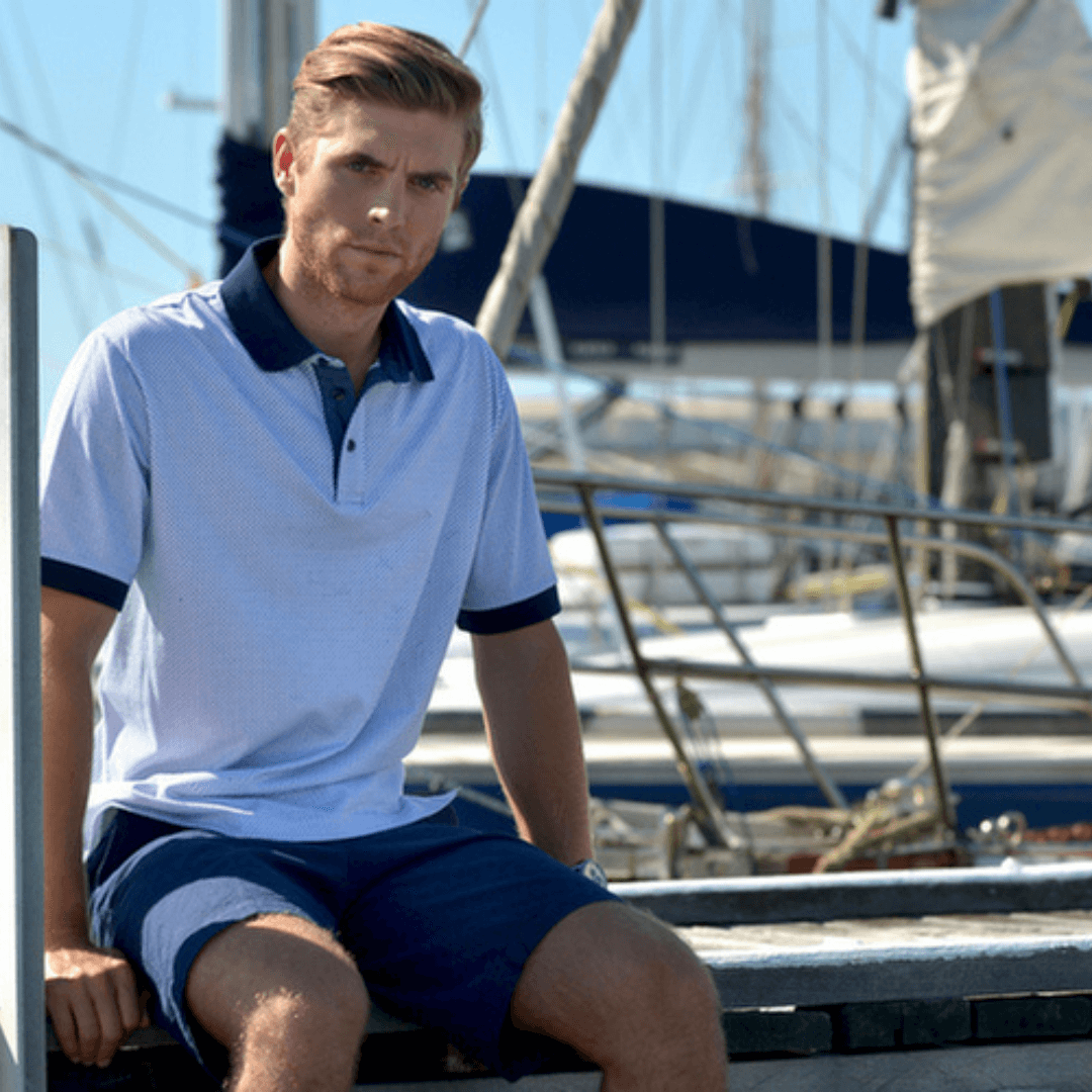 Stewarts Menswear Le Short fine check stretch cotton shorts. Lifestyle photo features man wearing shorts and a polo shirt sitting on a yacht.