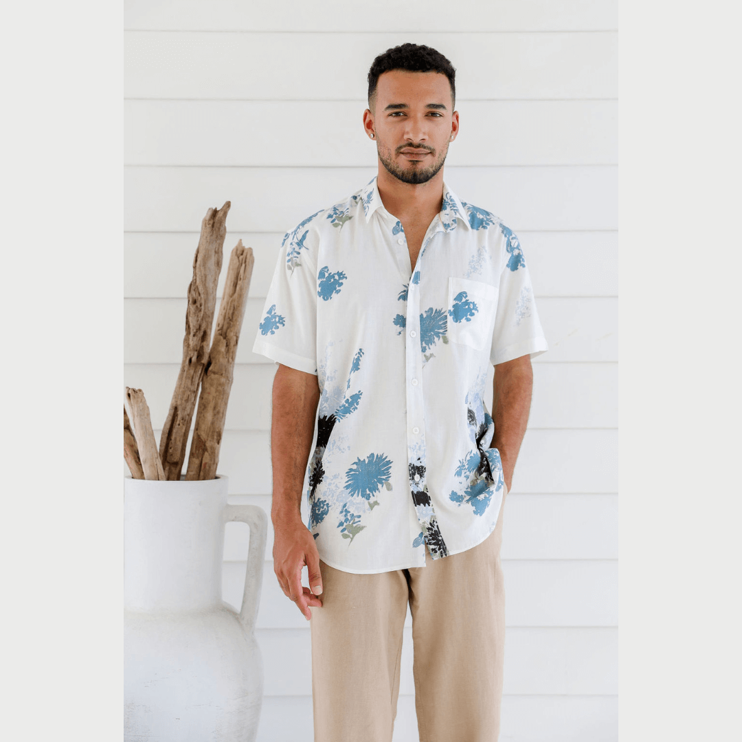 Male model wearing hemp/bamboo floral printed short sleeve shirt. Colour is white with blue/black/grey floral print.