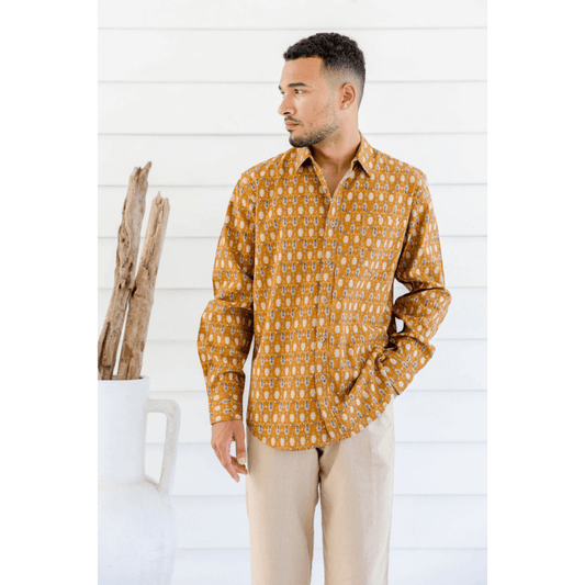 Male model is wearing a Hemp/cotton blend men's long sleeve shirt. Mustard colour with paisley like print all over. Print colours are navy, skyblue and white. Front view.